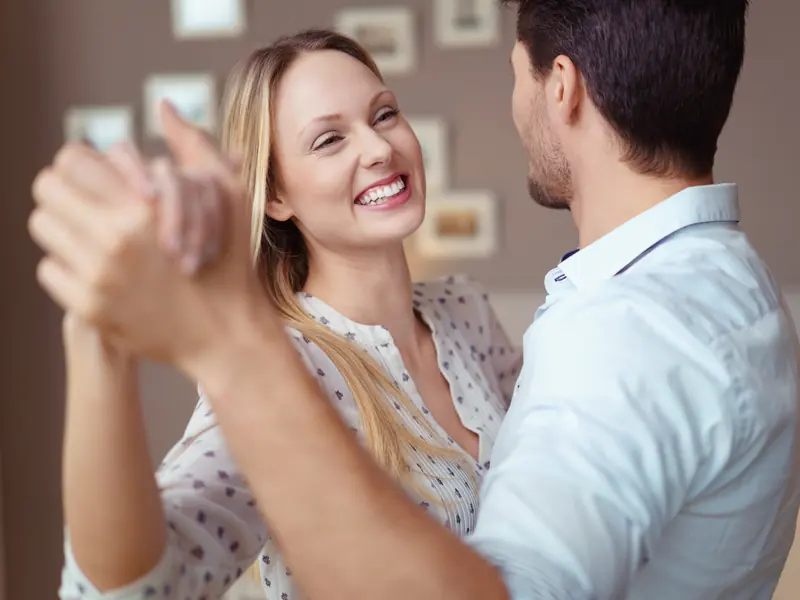 A smiling woman dancing hand in hand with her partner at home