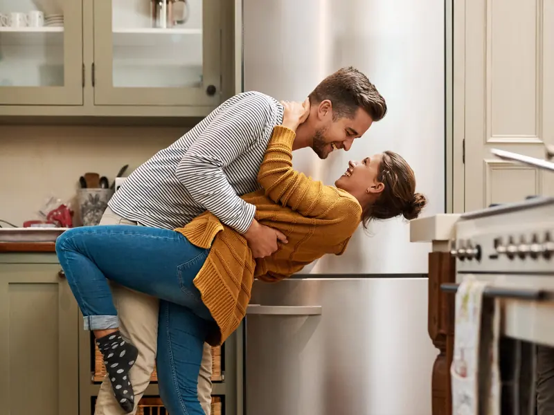 A smiling couple dancing in their kitchen, the man dipping the woman