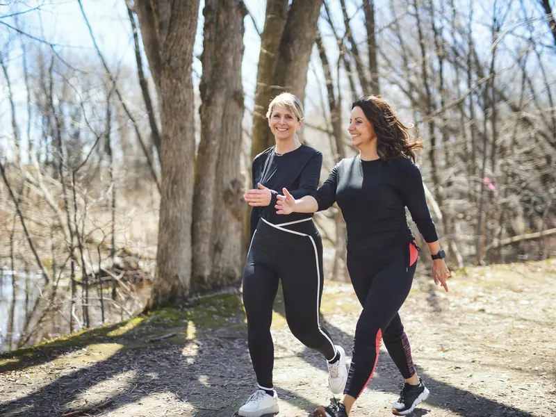 Two women walking briskly and chatting on a sunny woodland path