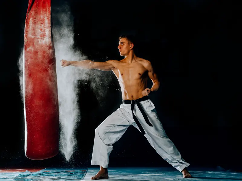 A karate black belt throwing a straight punch at a red heavy bag in a cloud of chalk