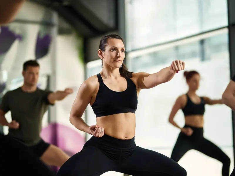 A focused woman throwing a straight punch in a karate-style fitness class with others training behind her