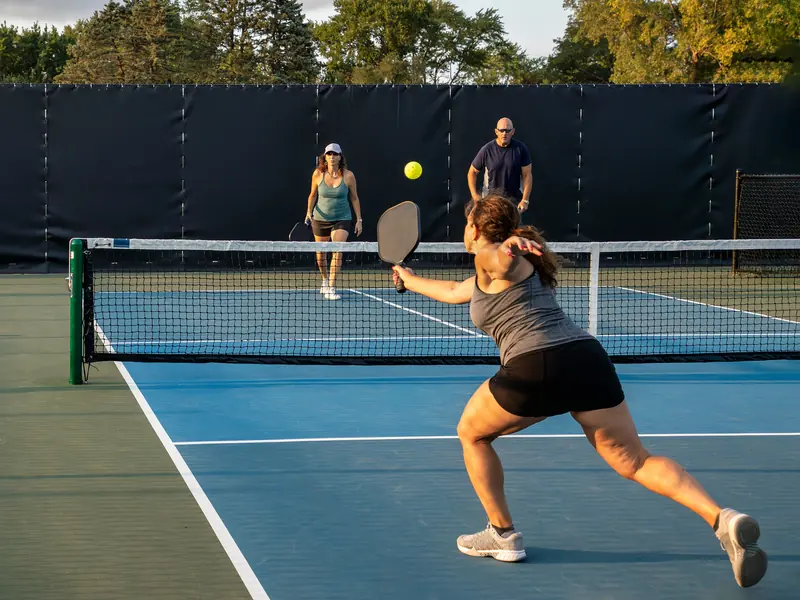 A woman lunging for a backhand return as a mixed doubles pair waits across the net