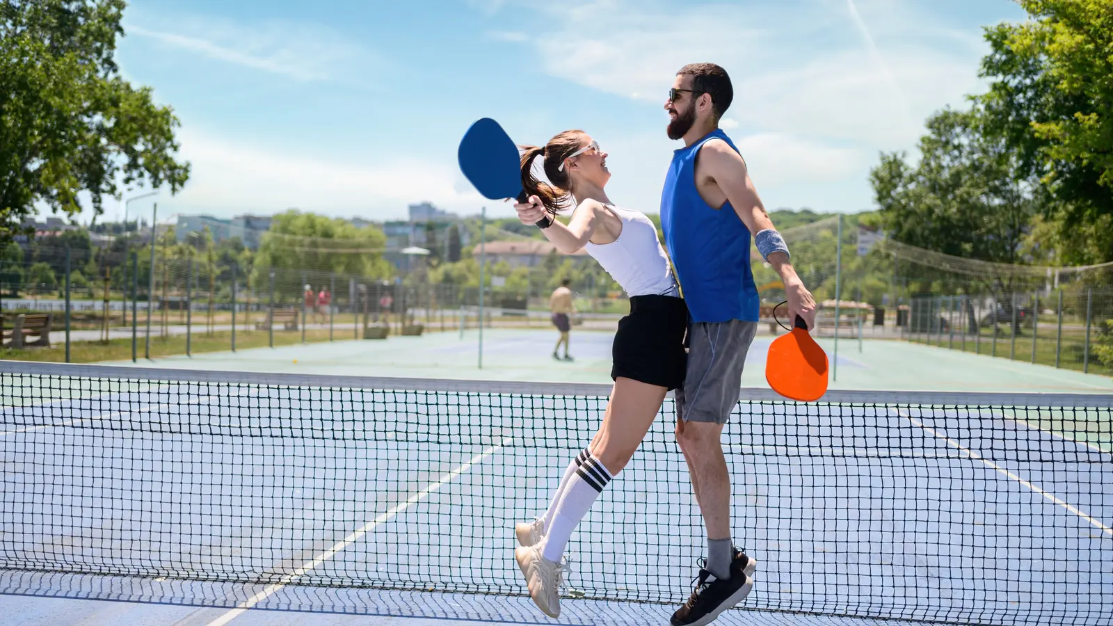 A happy couple jumping together at the net, celebrating a point on a sunny pickleball court