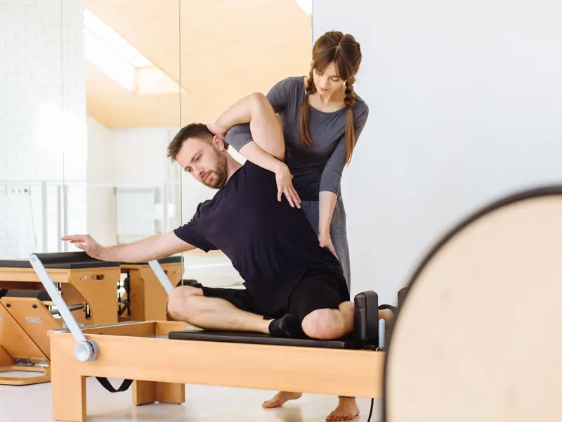 A Pilates instructor guiding a man through a twist on a reformer