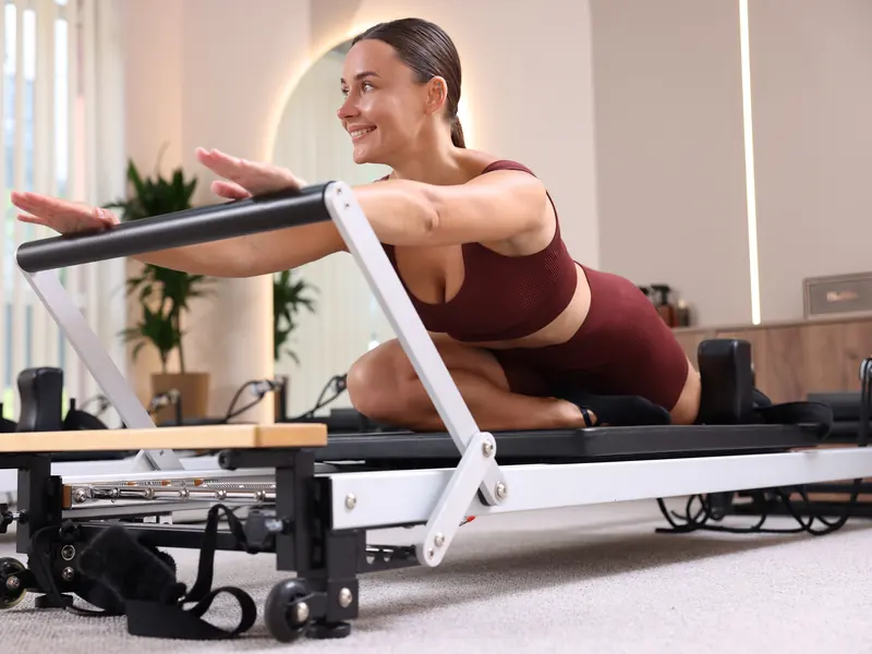 A smiling woman stretching forward on a Pilates reformer
