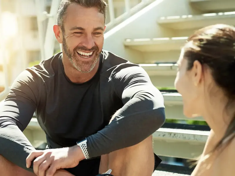 A smiling man in his 40s chatting with a woman on outdoor stairs after a workout