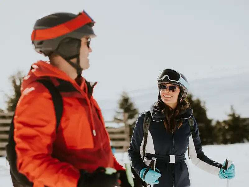 A smiling man and woman in ski gear chatting on a snowy slope