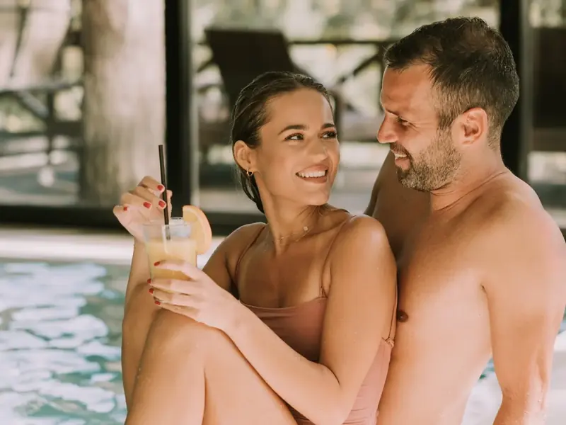 A laughing couple sitting together on the edge of an indoor pool