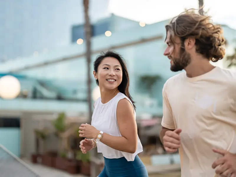 A smiling woman and man jogging side by side along a city waterfront