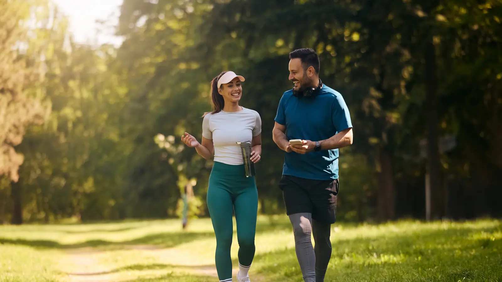 A smiling man and woman walking and chatting along a sunny park path