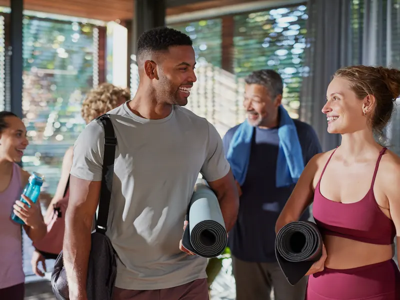 A mixed-age group carrying yoga mats, chatting and laughing after class