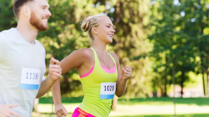 A smiling man and woman running side by side through a sunny park