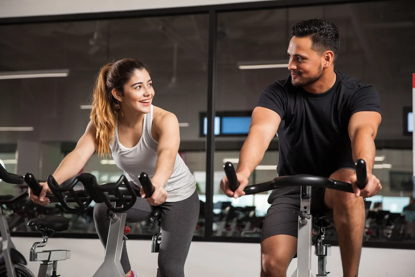 A woman and man smiling at each other while riding side by side in a spin class
