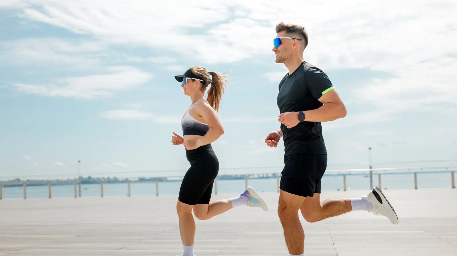 A couple running side by side along a sunny seaside promenade