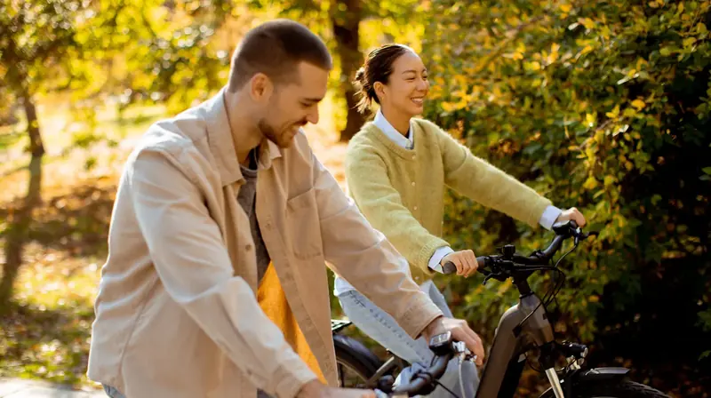 A smiling couple riding e-bikes together through autumn woods