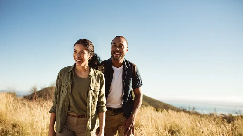A smiling couple walking hand in hand through golden grass on a sunny day