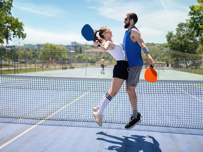 A man and woman leaping to celebrate a point together on an outdoor pickleball court