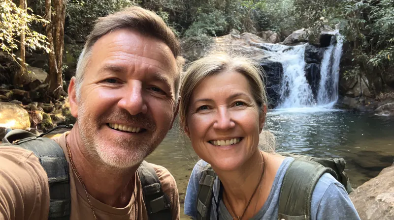 A smiling middle-aged couple taking a selfie by a waterfall on a hike