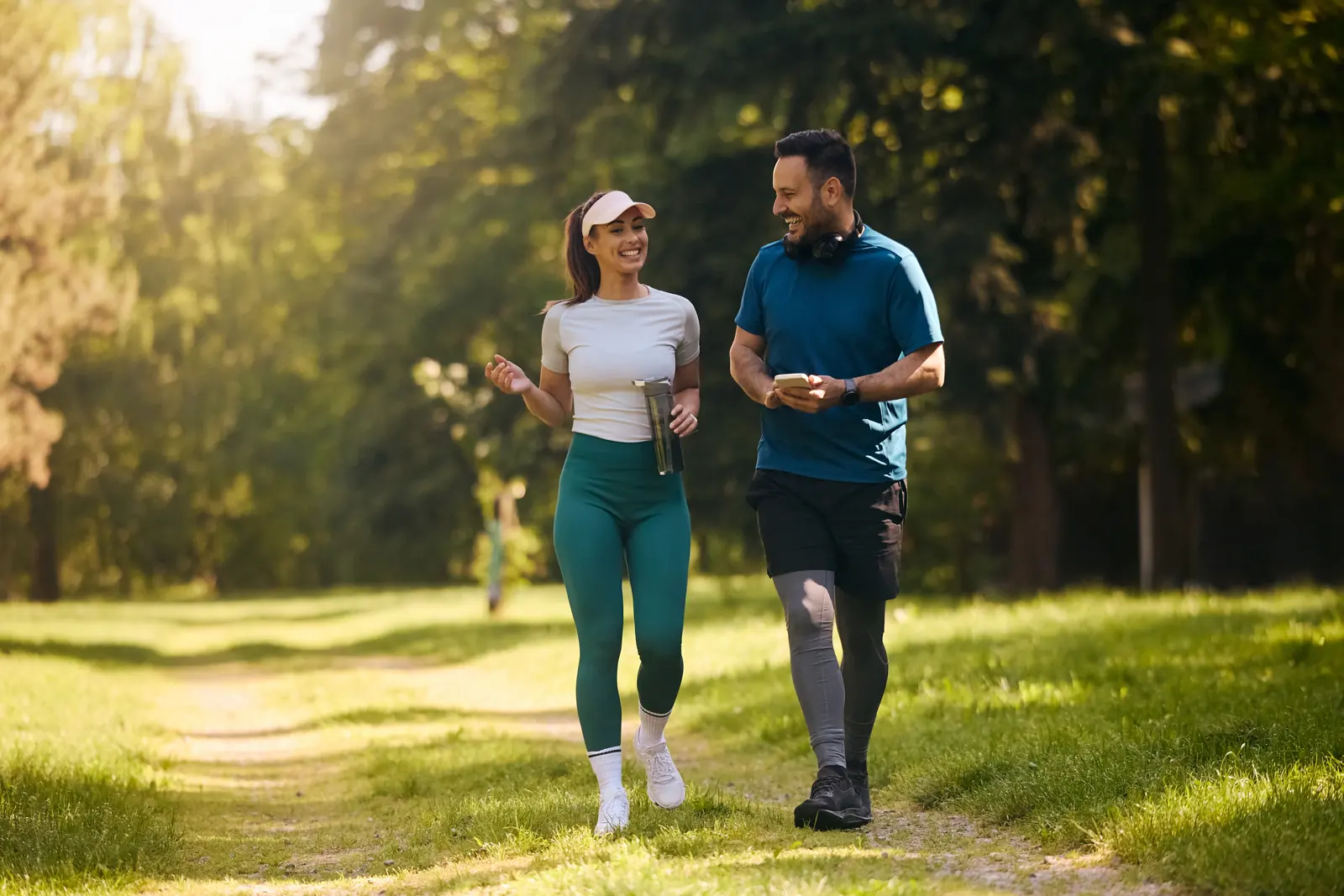 A smiling couple in workout clothes walking together along a sunny park path